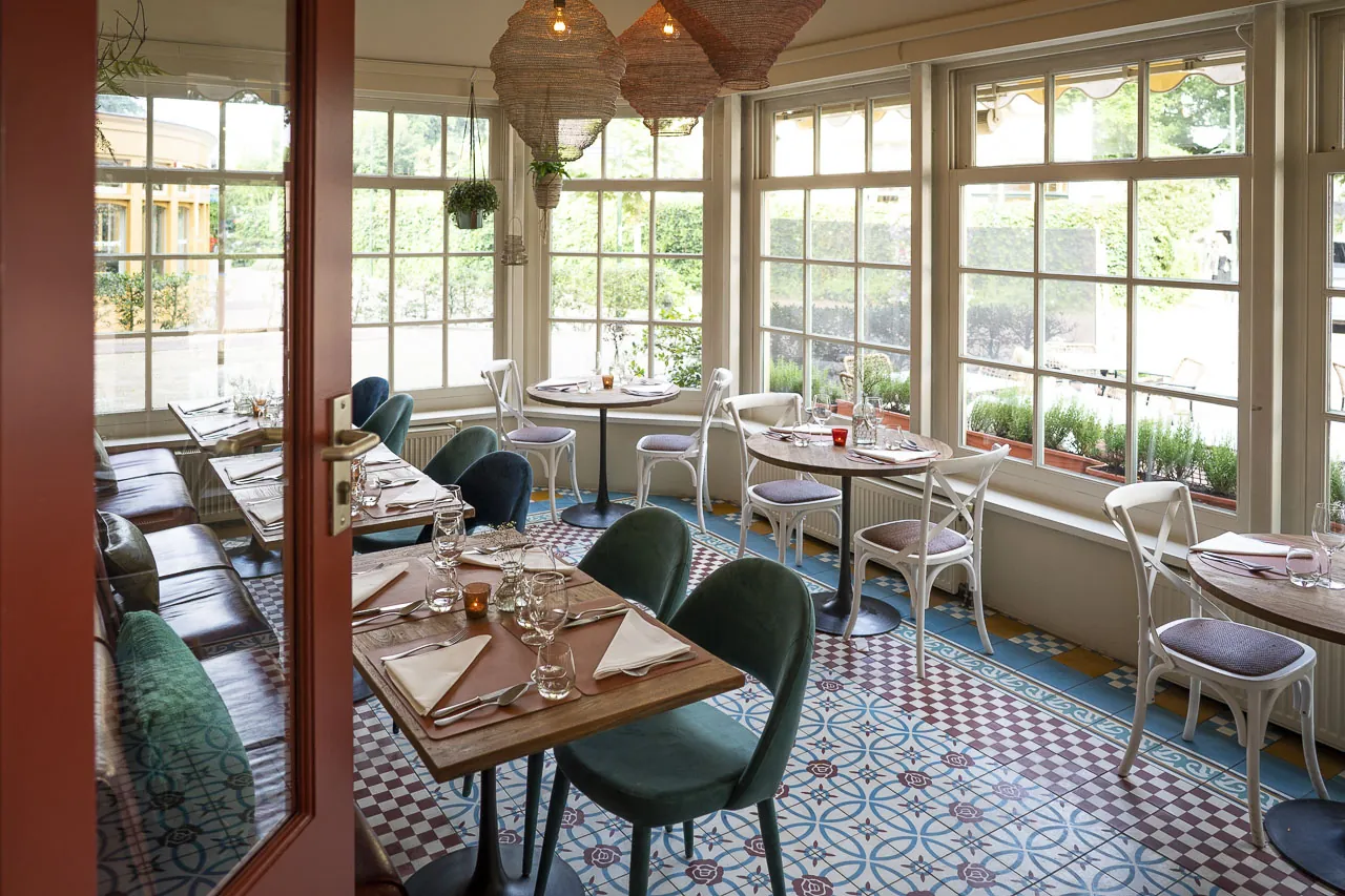 De eetzaal van Maximiliano met groene stoelen en wit gedekte tafels bij de ramen